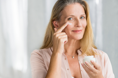 smiling senior woman applying anti-aging lotion to remove dark circles under eyes